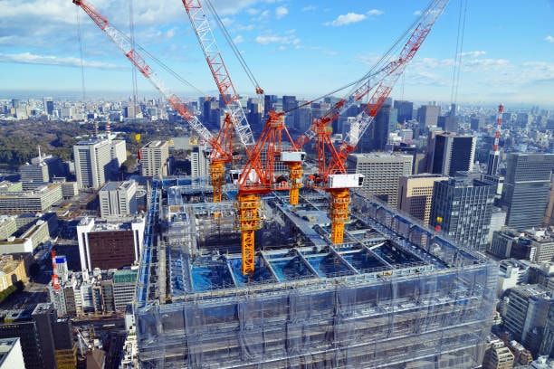 Aerial view of commercial high-rise construction with multiple tower cranes and safety netting