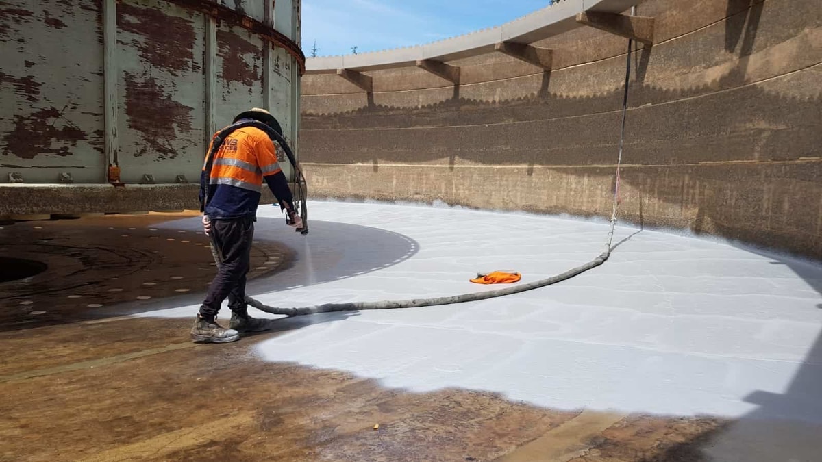 Worker applying spray foam roofing to commercial flat roof with professional equipment