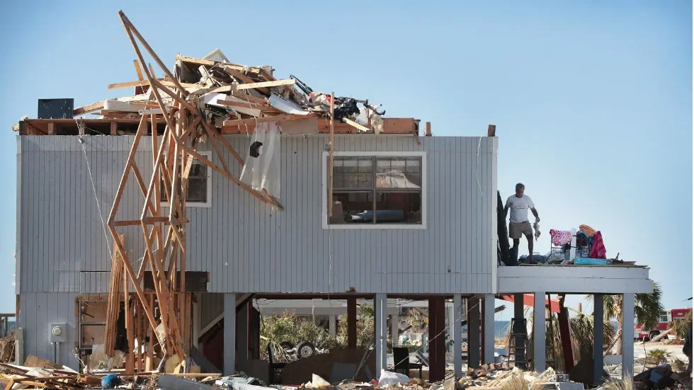 Severe wind damage to elevated home roof with workers inspecting destruction